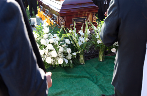 A coffin being lowered into a grave, surrounded by bunches of white flowers